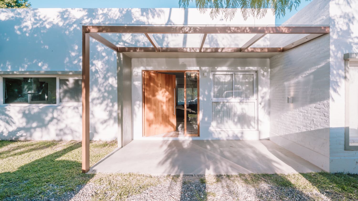 Frente de la casa con pérgola de madera y vidrio